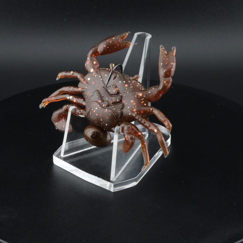 1.3 in plastic crab lure on clear block, brown body with orange legs and glitter specks