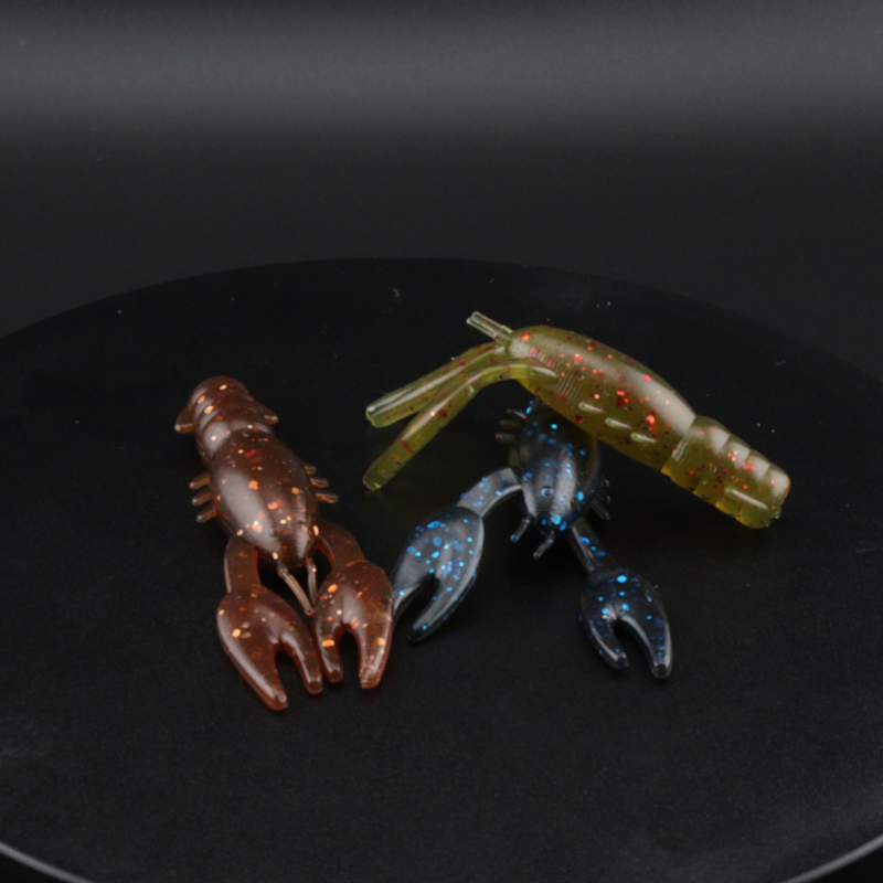 Soft plastic craw lures in dark brown, green, and blue, with clawed legs